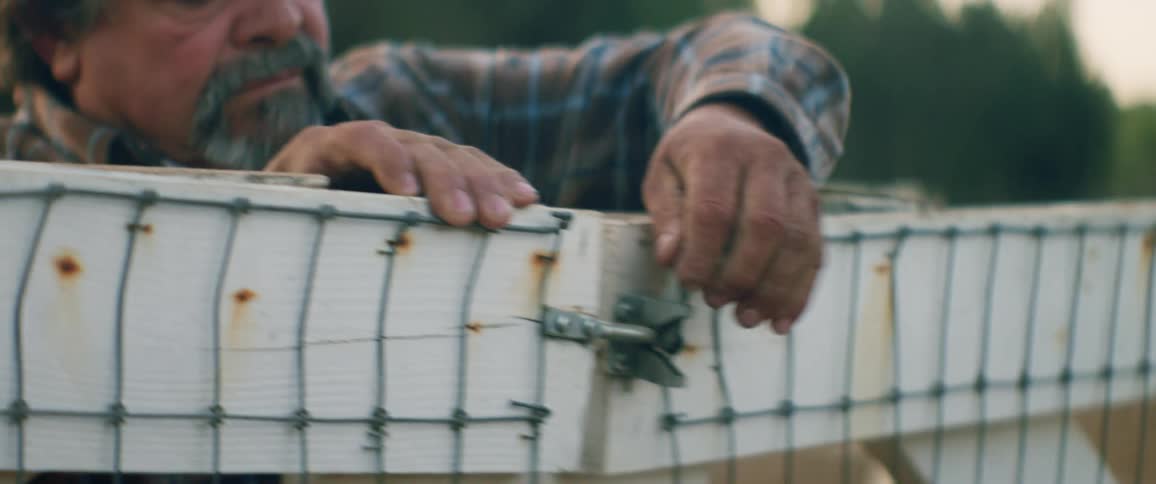 A man struggles with the lock on a gate of a high outdoor fence