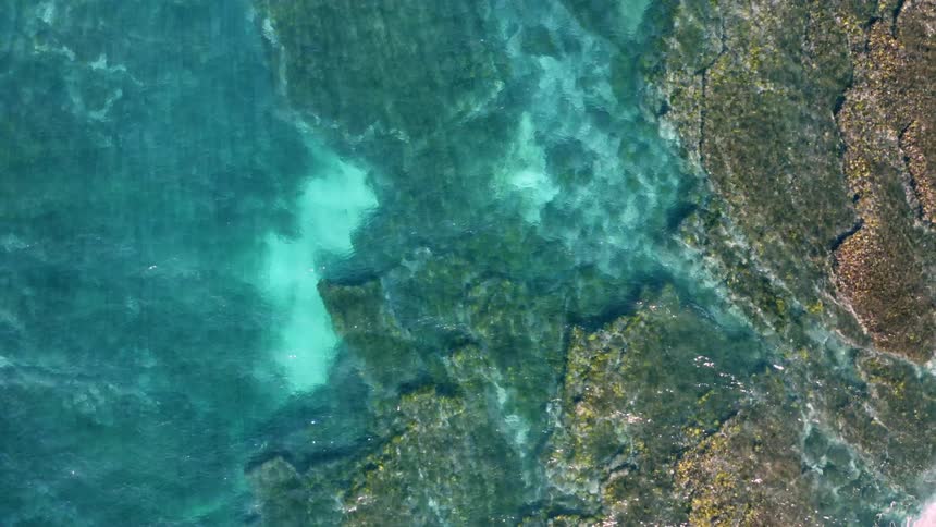 An aerial view of a clear blue waterway and rocks