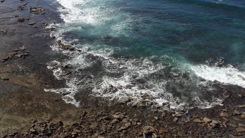 Ocean waves wash into the rocky shore on a sunny day