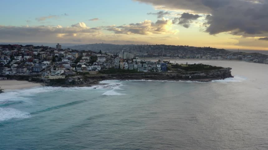 Waves crash against beach and seawall of city under yellow tinted sky
