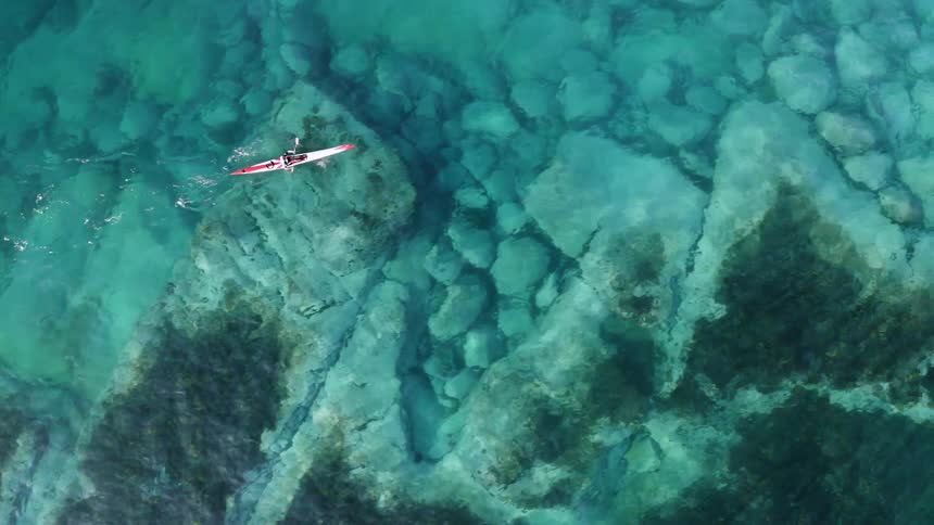 A person in a kayak paddles across the ocean during the day