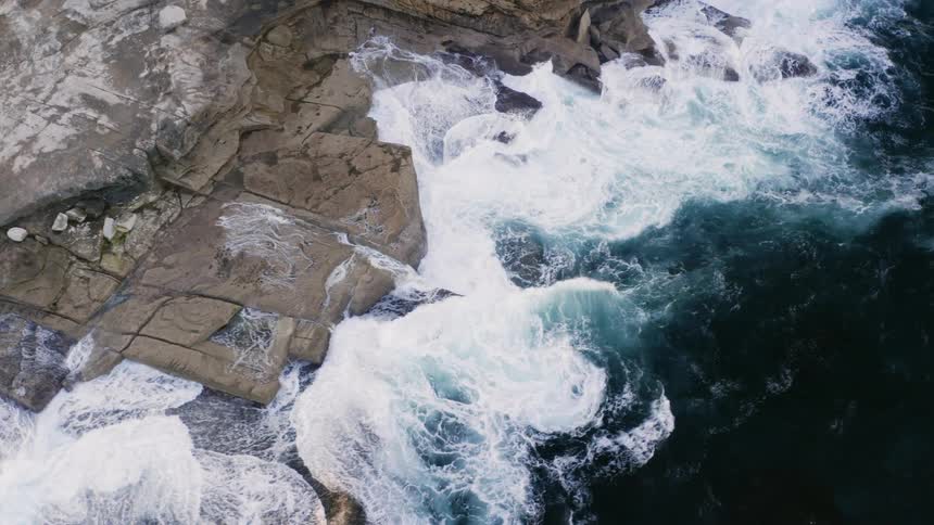 Aerial view of ocean waves crashing against cliff rocks
