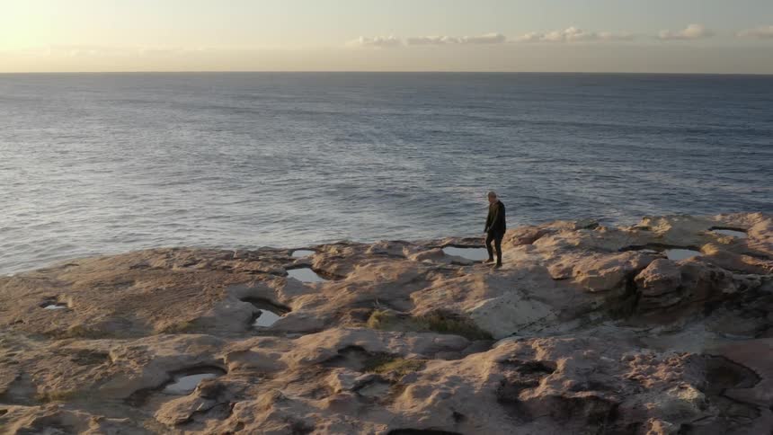 An aerial view of a person jumping rope on a large rock next to the sea