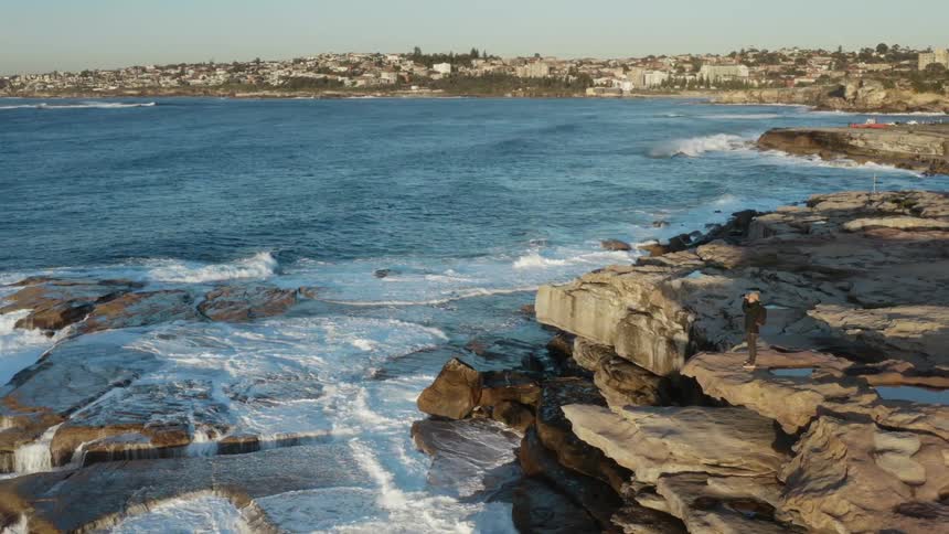 A man stands on a cliff overlooking an ocean near dense neighborhoods