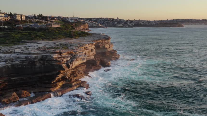 Aerial view of foamy ocean waves breaking against a rocky promontory overlooking the bay