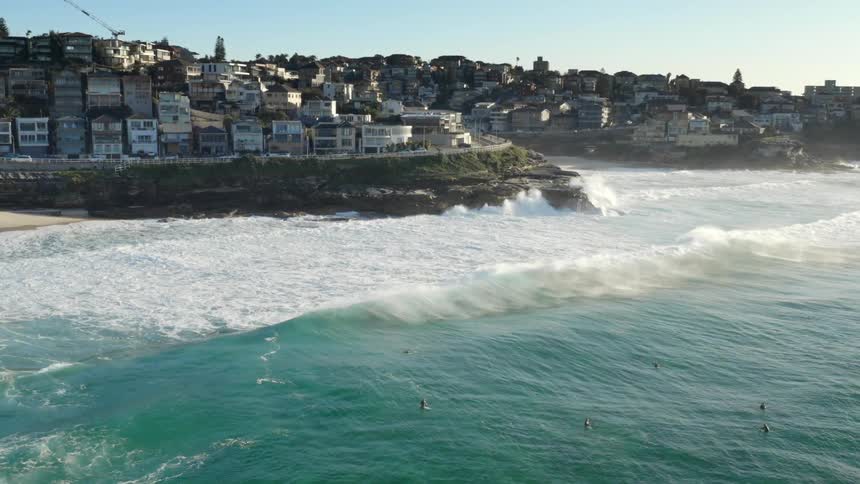 Ocean waves roll into the coast below a city on a sunny day