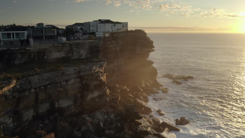 Buildings on a sheer stone cliff over the ocean in the evening
