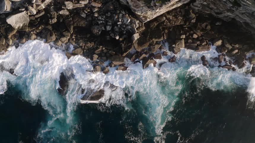 Aerial view of foamy ocean waves crashing against a cliff