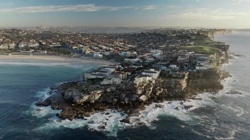 Ocean waves crash into a rocky headland on the edge of a sunny during the day