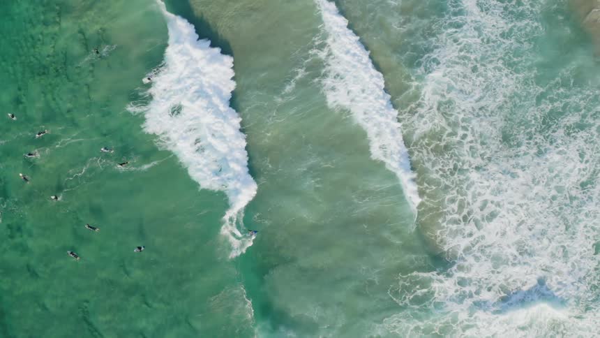 A turquoise ocean is dotted with people swimming laying on surfboards and riding strong waves