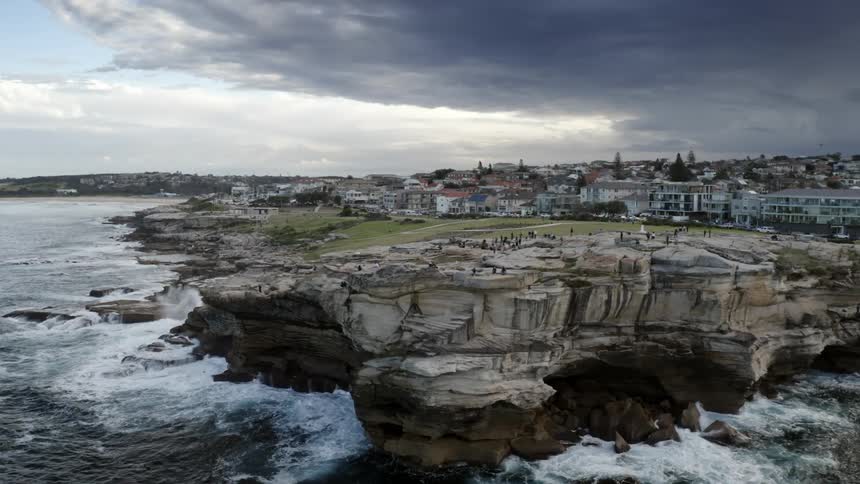 People relax on a stone cliff above the ocean on the outskirts of a metropolis on a cloudy day