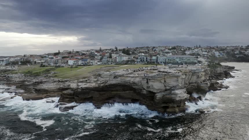An aerial view of people standing on a cliff on the shore in front of a neighborhood