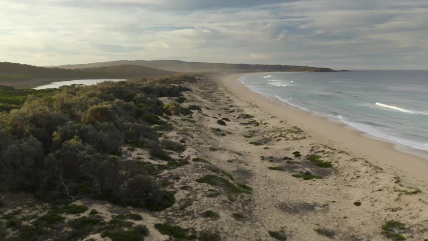 An aerial view of ocean waves flowing towards a sandy beach