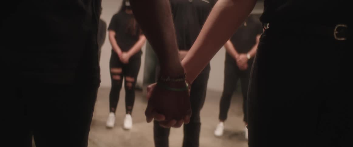 Couple holds hand facing others wearing similar clothing and face masks
