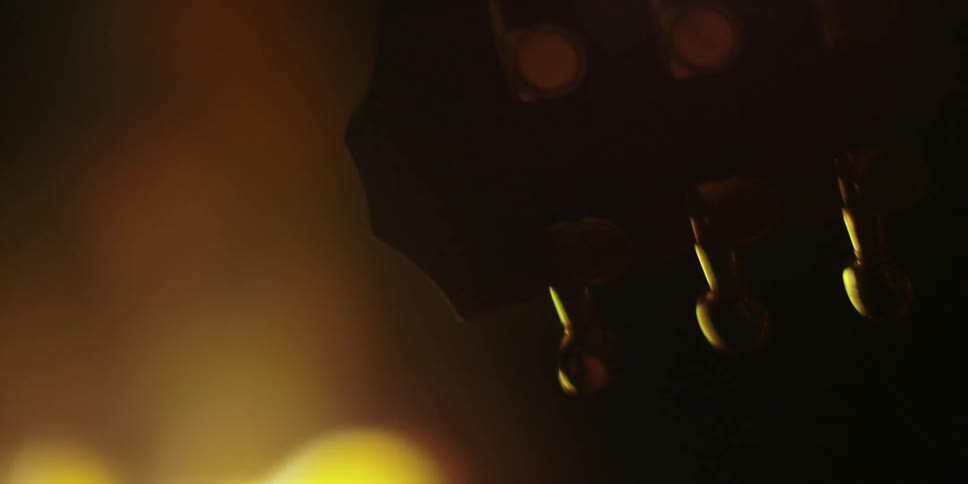 Close up of the top of a guitar with a fire going on behind it
