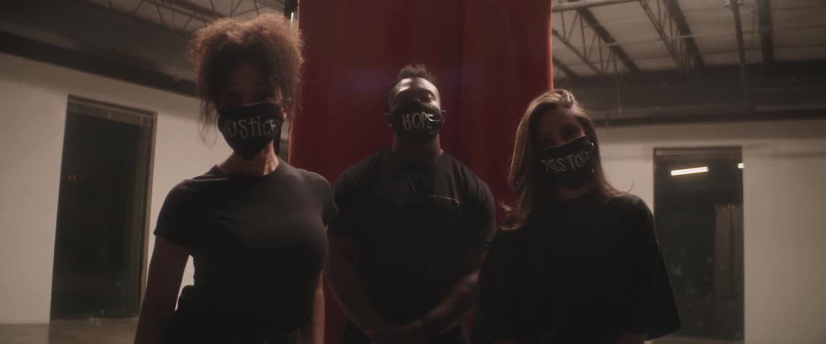 Three people are standing while wearing face coverings with social messages printed on them