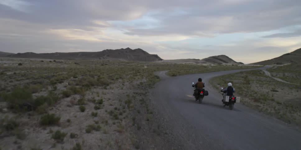 Two people ride motorcycles down an abandoned country road