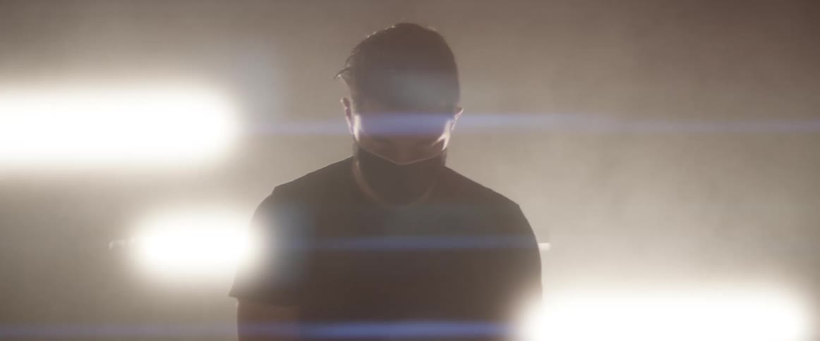Man wearing face mask stands on a dark room in front of flashing fluorescent lights