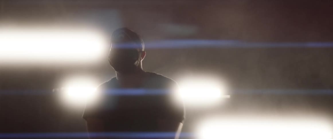 Man wearing a covid mask stabs his arm in the air while standing in front of some lights