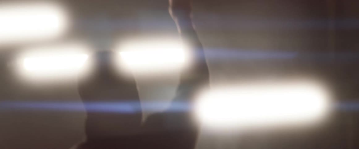 A silhouette of a person with their hand up with lights flickering in the background