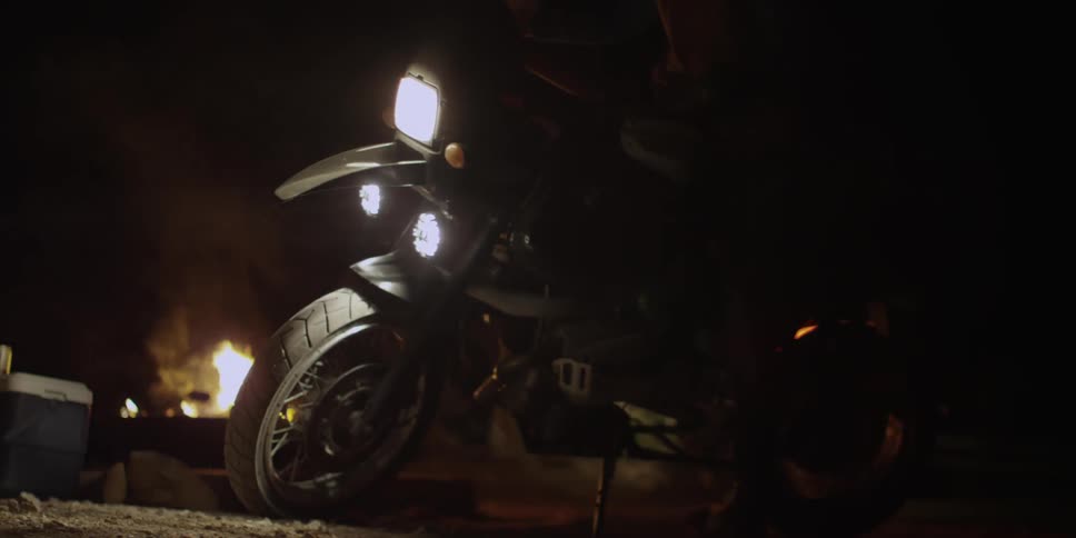 A motorcyclist parking his bike next to a campfire