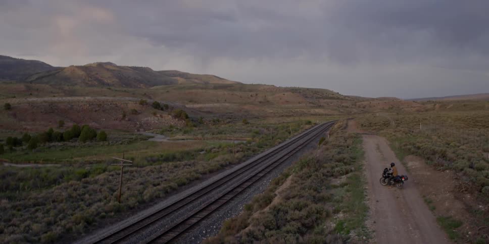 A motorcycle rider pulls to the edge of the road overlooking railroad tracks