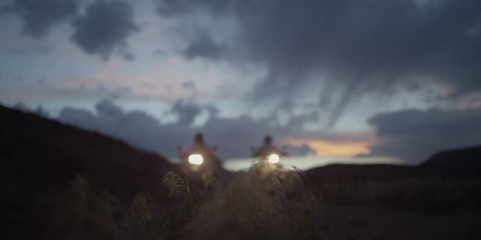 Two motorcycles drive forward at sunset