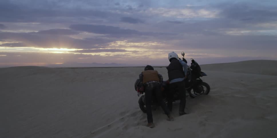 Two people pick up a fallen motorcycle in the desert
