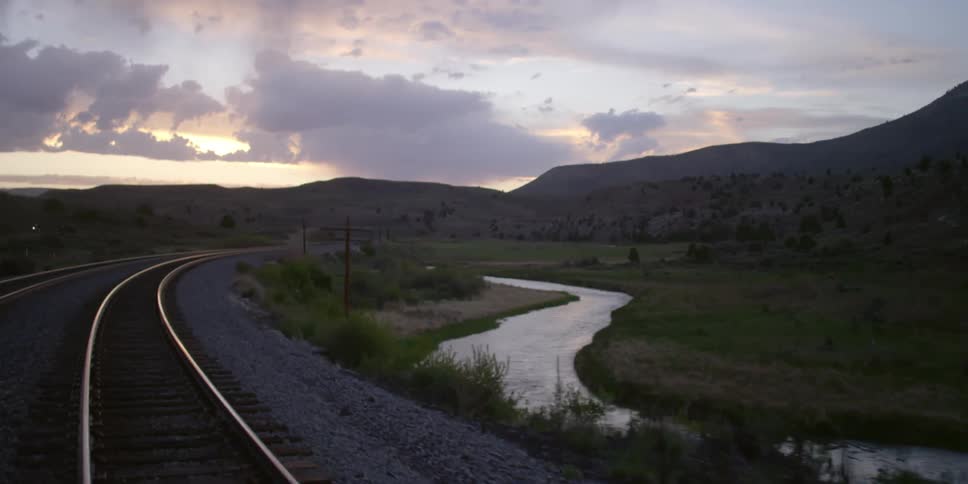 Train tracks next to a river on a cloudy day