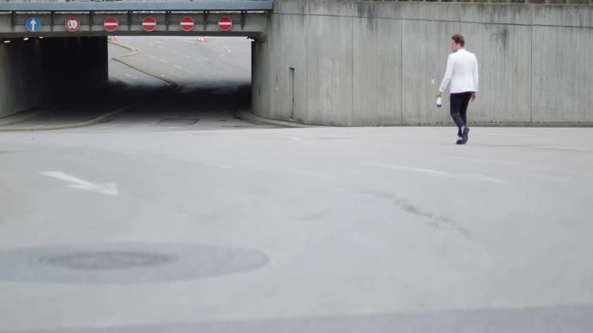 A man with a white blazer walking with a bottle in his hand
