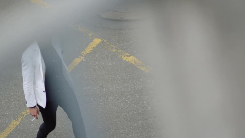 A man walks across a parking lot smoking a cigarette and holding a wine bottle