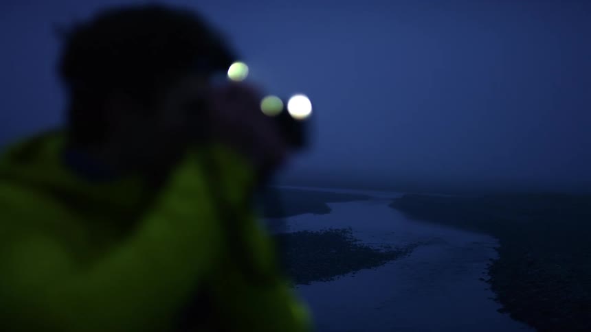 A man standing above a river at night takes a photo