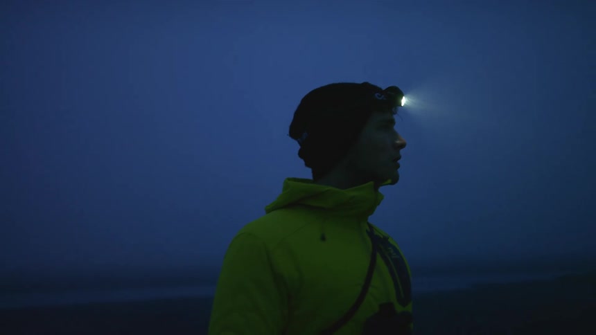 A young man with a headlight on looks across the landscape at night
