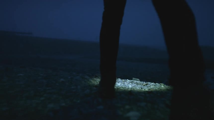 A person walking over rocky ground with a flashlight at night