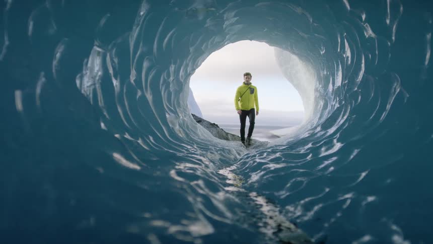 A man walking into an ice tunnel with the sky and clouds in the background