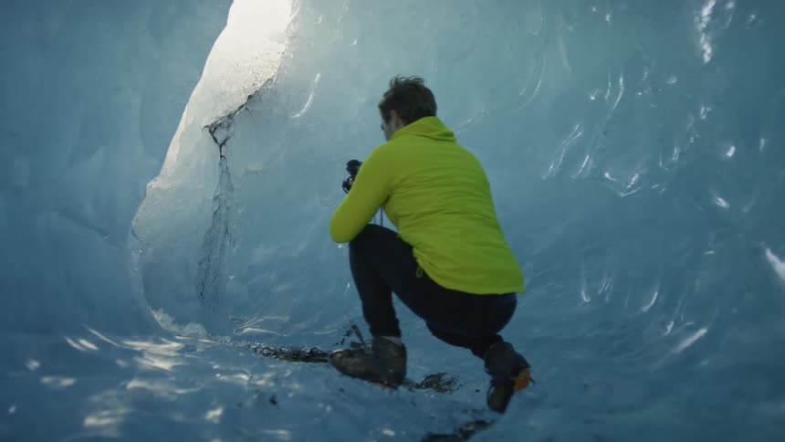 A man with a camera and a hoodie stooping down in an ice tunnel