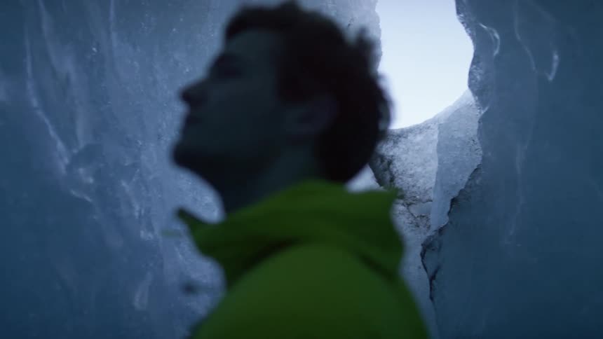 A man stands in an ice cave and touches the walls and looks around