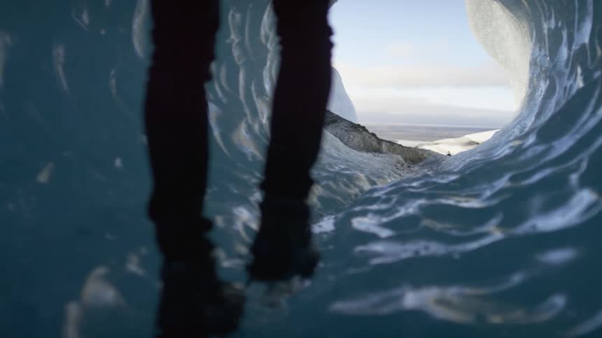 A hiker walks through a narrow tunnel of ice on a sunny day
