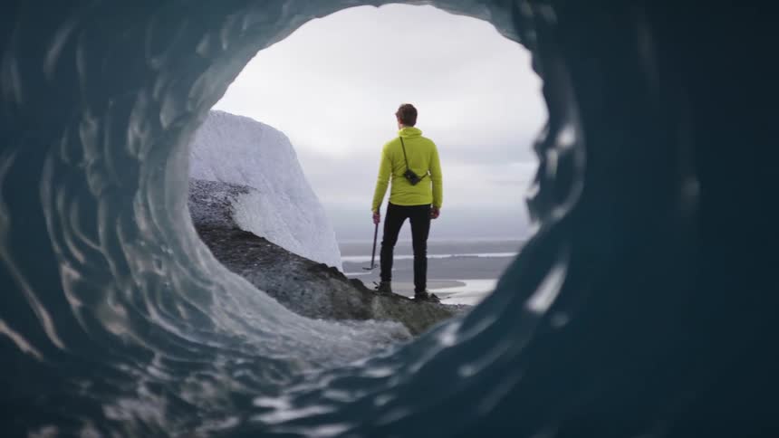 A man holding an ice pick stands on the shore next to an iceberg