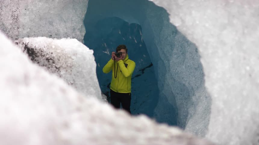 A man in an ice cave taking a photo with a camera