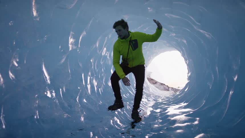 A man stands in an ice cave and touches the walls and looks around