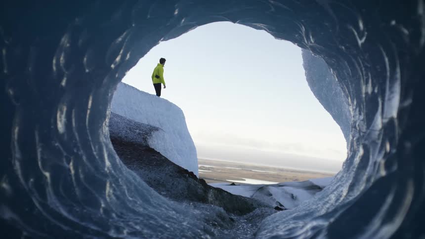 A person walking in front of a cave on a snowy mountain