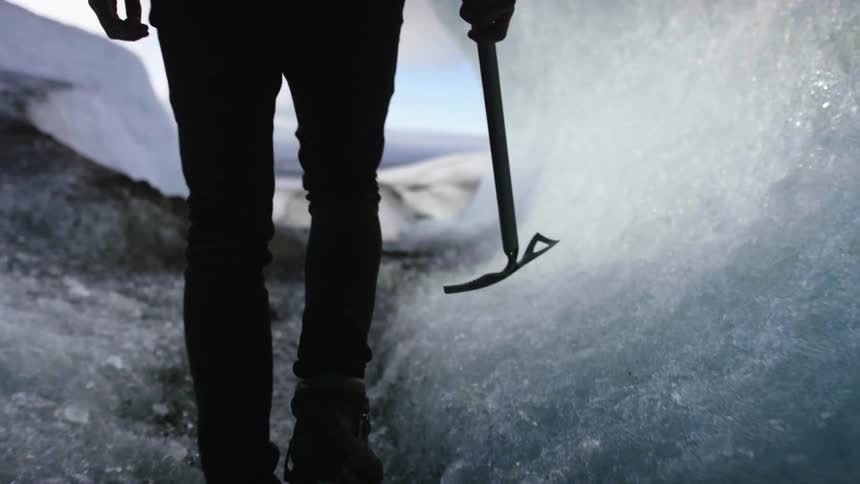 A man carrying a pick ax is walking through an icy tunnel on an icy and rocky landscape