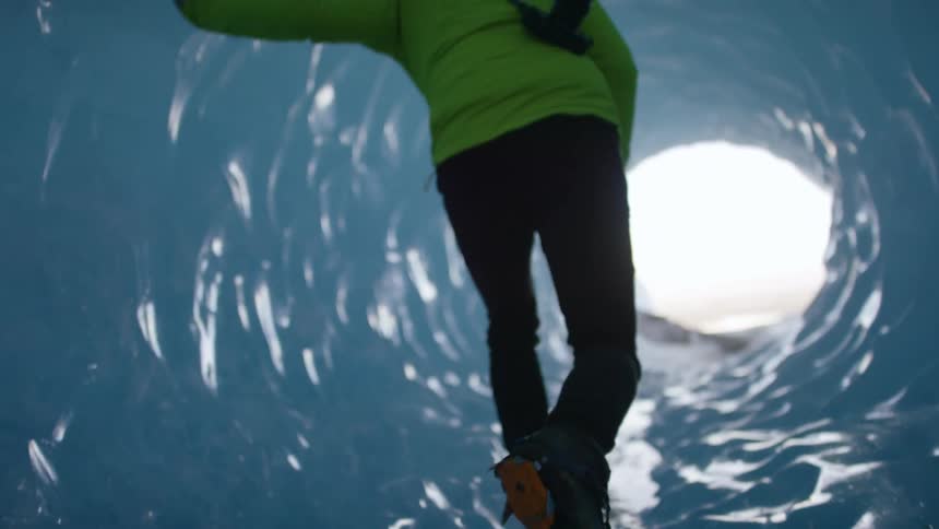 A man with a camera walking in an ice tunnel with the sky in the background