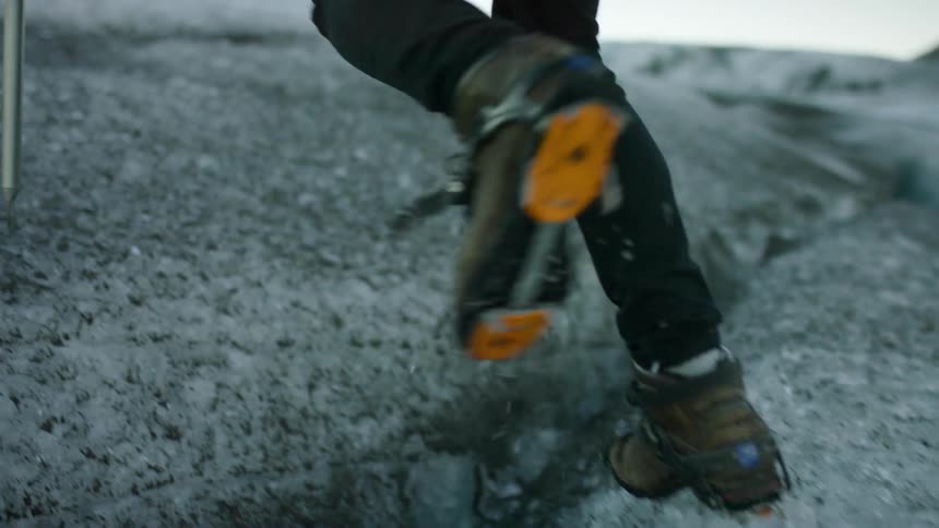A person with a metal rod walking on ice with cleats with the sky and clouds in the background