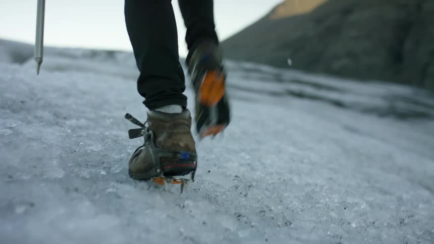 A person wearing climbing spikes boes up an ice covered slope in the mountains at morning