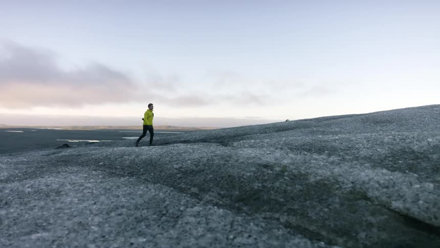 Man walks up slight incline with glints of water showing on land toward horizon