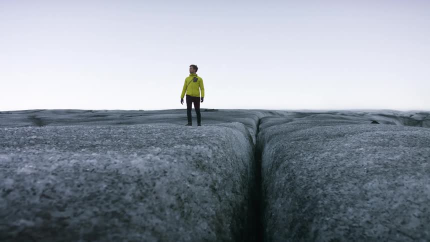 A man walking looks down at a large crevice in a rocky area