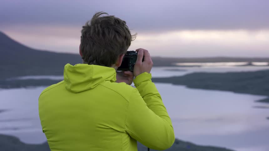 A man standing on the shore takes a picture of the water