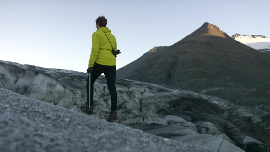 A man with a camera and gloves walking with a mountain range and the sky in the background